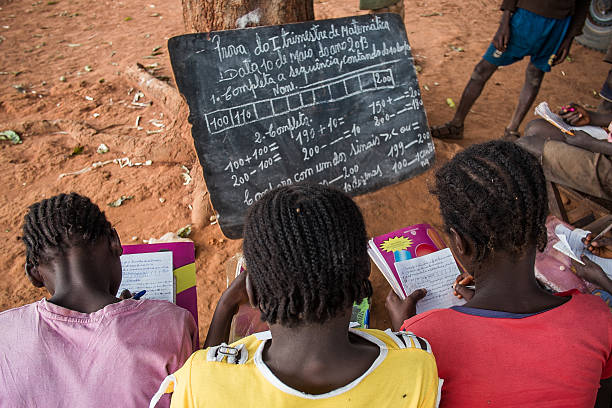Bie, Angola - May 10, 2013. Three girls undertake a maths exam by a tree in a rural school. Access to education in low income countries of sub-saharan Africa is one of the challenges of the global community, as stated in the Sustainable Development Goals.